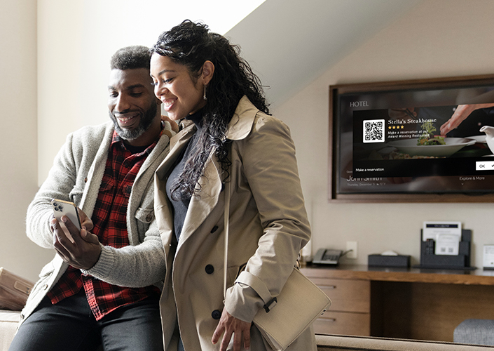 A man and woman use a cell phone to book a restaurant reservation after using the hotel's in-room TV from SONIFI